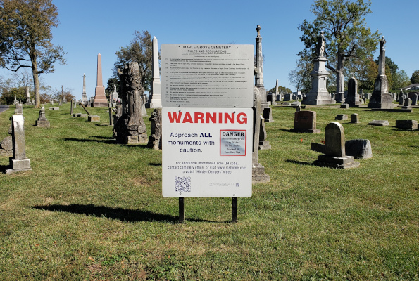 A large warning sign mounted below the cemetery's own Rules and Regulations sign
