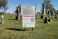 A large warning sign mounted below the cemetery's own Rules and Regulations sign