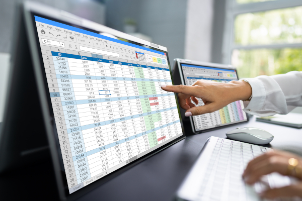 A woman pointing at one of two computer screens that display data