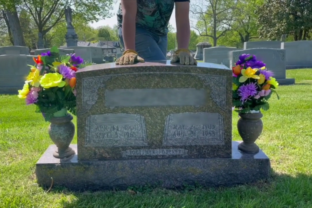 A man in work gloves, hands resting on a granite monument