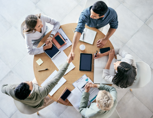 Business people collaborate around a table. A handshake signals agreement